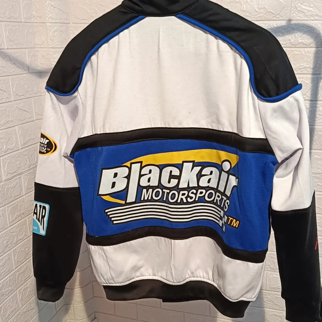 Black bike racer jacket by BlackAir, decorated with striking white prints and text. The design includes a stand-up collar, zip-up front, and multiple graphic elements across the chest, sleeves, and back.