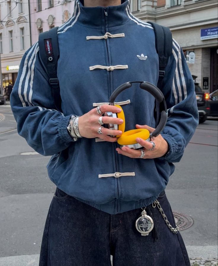 Person wearing a blue CNY jacket holding a yellow object on a city street.