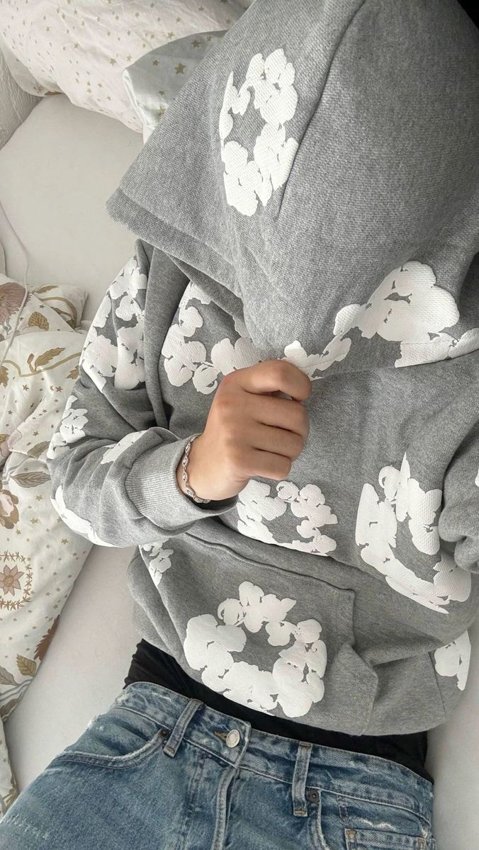 Person wearing a gray hoodie with white floral patterns sitting on a couch.