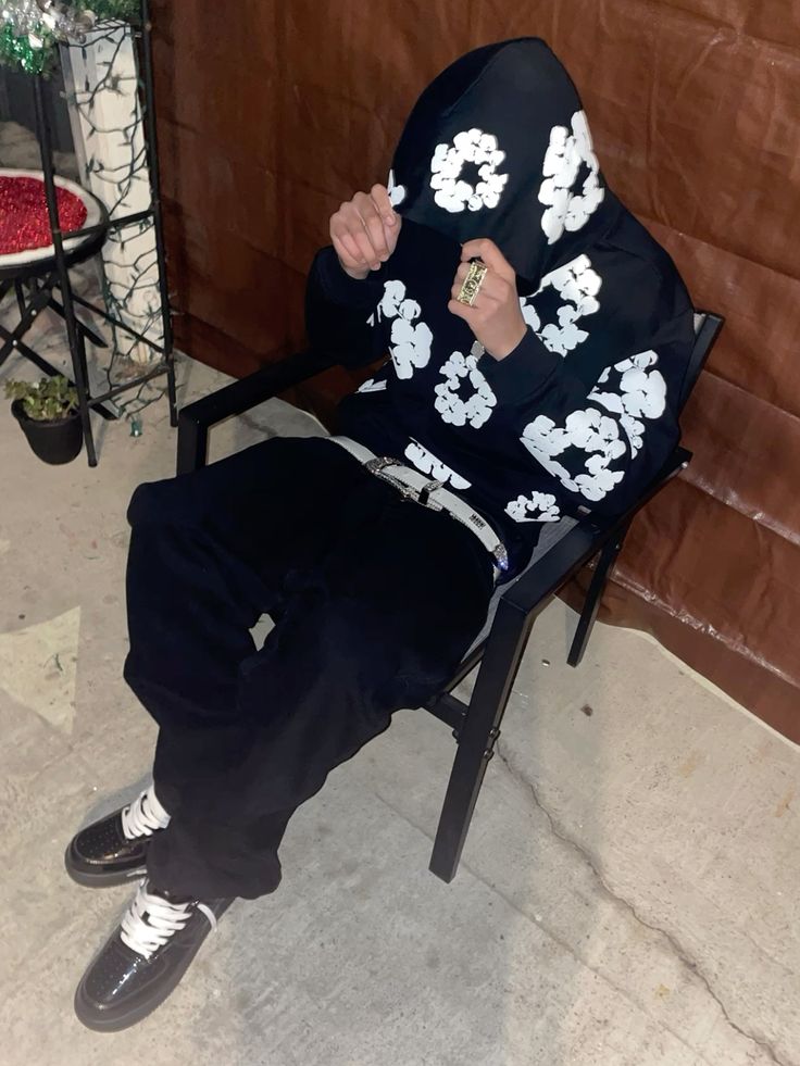 Person wearing a black hoodie with white floral patterns sitting on a chair.