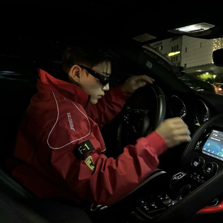 Person wearing a red Ferrari jacket sitting inside a car at night.