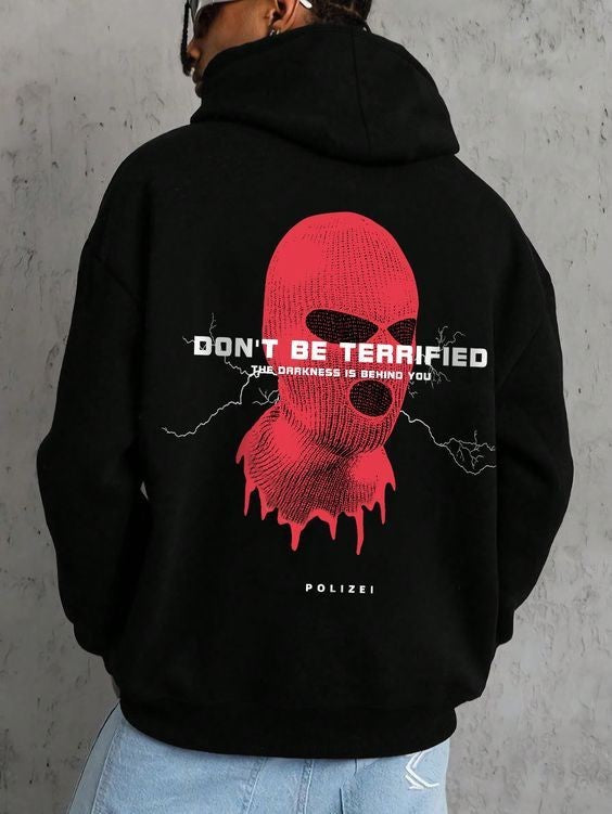 A person wearing a black hoodie with a red and white ski mask print and the text 'DON'T BE TERRIFIED' on the front.