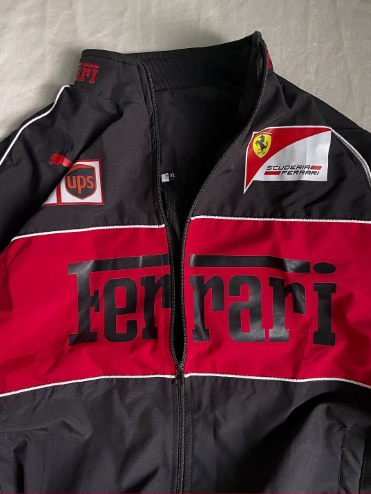 Black and red Ferrari jacket with various logos on a gray background